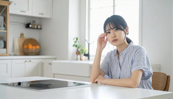 疲れた表情でキッチンに座る若い女性の写真