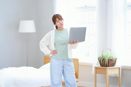 腰に手を当てパソコンを見る女性の写真