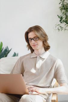 座って膝の上でノートパソコンを使う微笑む若い男性 男性,外国人,欧米人の写真素材