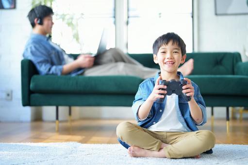 コントローラーを持っている男の子と後ろでヘッドフォンをしてパソコンを見ている男性 コントローラーを持っている男の子と後ろでヘッドフォンをしてパソコンを見ている男性の写真