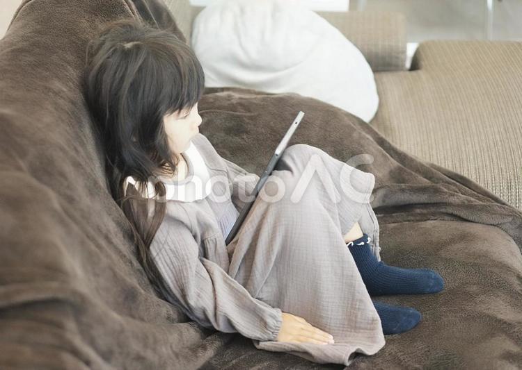 ソファーに座ってタブレットを見る女の子 子供,女の子,タブレットの写真素材