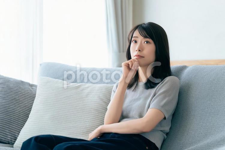 ソファに座って考えごとをする女性 女性,考える,困るの写真素材