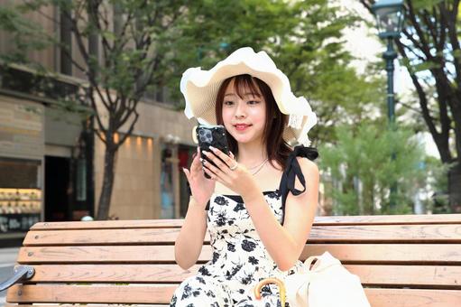 ベンチでスマホを見る女性 ベンチでスマホを見る女性 女性,スマートフォン,ベンチの写真素材