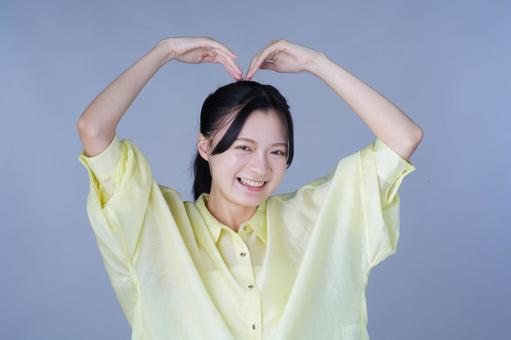 ハートポーズを作る黄色い服の女性 女性,笑顔,笑うの写真素材