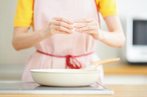 フライパンの上で卵を持つ手元の写真