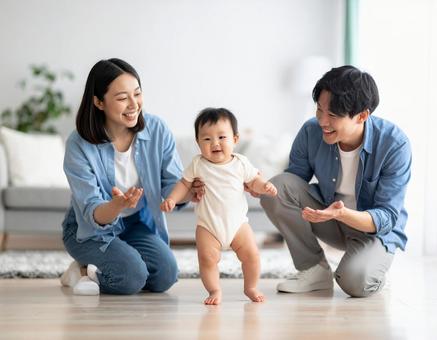初めて歩いた赤ちゃんと見守る若い両親 初めて歩いた赤ちゃんと見守る若い両親の写真