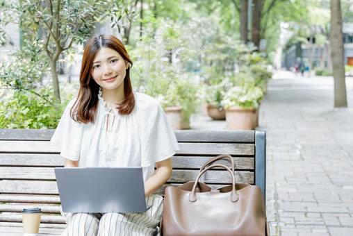 ベンチでノートパソコンを使う笑顔の女性 ノートパソコン,女性,日本人の写真素材