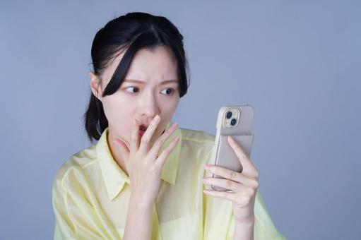 スマホを見て怪訝な顔の黄色い服を着た女性 女性,スマートフォン,持つの写真素材