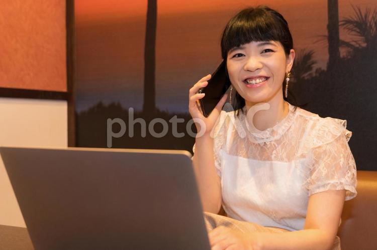 ノートパソコンと電話する女性 ノートパソコンと電話する女性 在宅ワーク,笑顔,スマホの写真素材