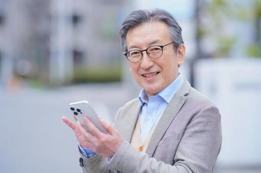 屋外でスマートフォンを操作するカメラ目線の高齢男性 男性,おじいちゃん,1人の写真素材