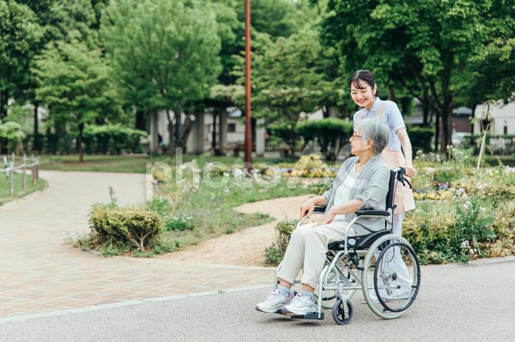 車椅子に乗った高齢者女性と女性スタッフ（花畑） 介護士,高齢者,看護師の写真素材