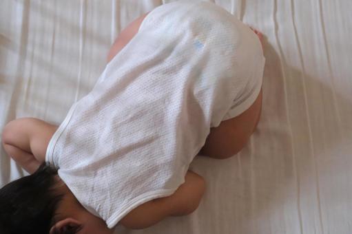 ベビーベッドでうずくまって寝る赤ちゃん ベビーベッドでうずくまって寝る赤ちゃんの写真