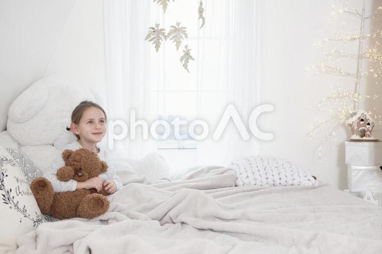 クマのぬいぐるみを抱っこしてベッドに座っている女の子 子ども,女の子,外国人の写真素材