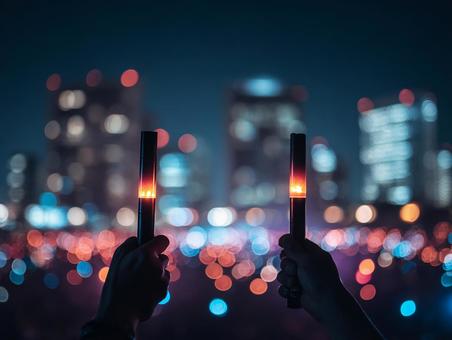 夜景を背景にしたペンライトを掲げる手 夜景を背景にしたペンライトを掲げる手の写真