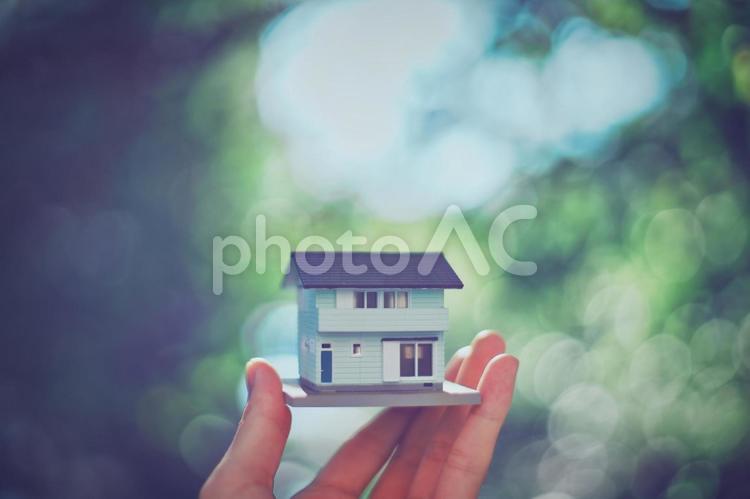 住宅模型を持つ人の手と緑ぼかし背景 家,住宅,住宅模型の写真素材