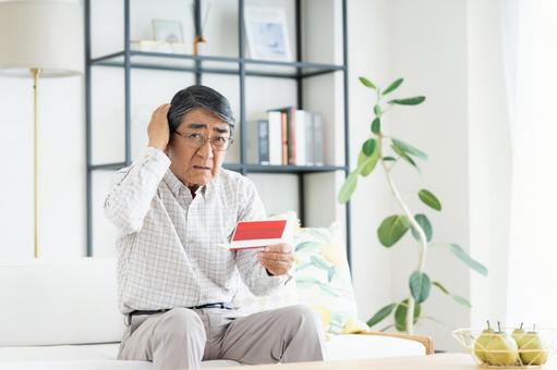 通帳を見て悩むシニアの男性 通帳を見て悩むシニアの男性の写真