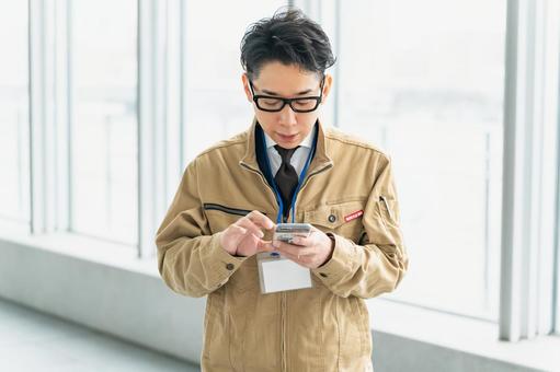 仕事中に携帯を確認する作業服の男性 仕事中に携帯を確認する作業服の男性 ビジネス,ビジネスマン,作業員の写真素材