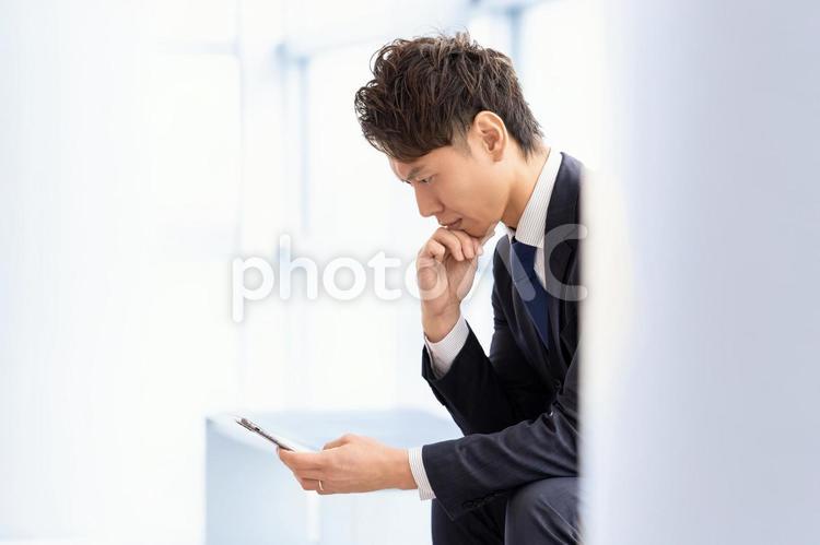 スマホを見て考える男性ビジネスマン 男性,ビジネス,ビジネスマンの写真素材