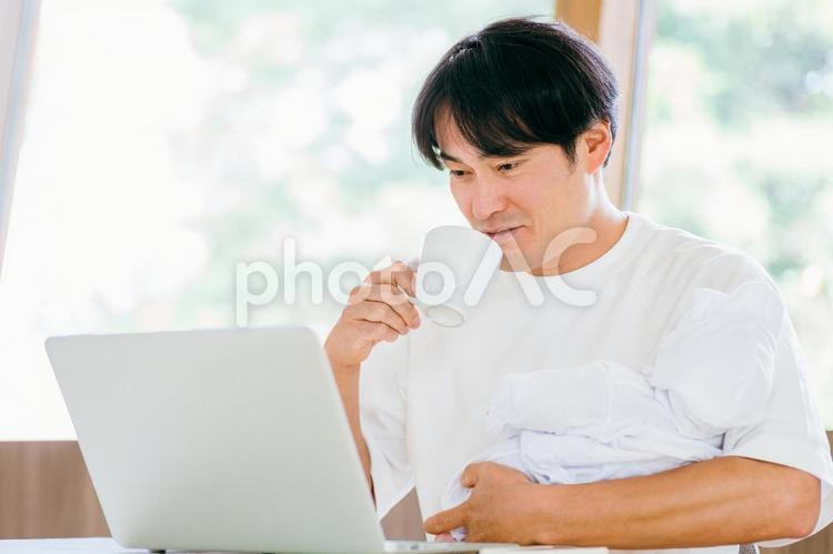 赤ちゃんを抱きながら仕事する男性 テレワーク,育児,リモートワークの写真素材