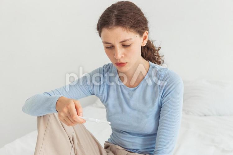 膝を立てて体温計を見ているポニーテールの女性 女性,人物,体温計の写真素材