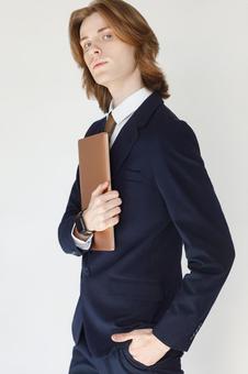 カメラ目線でポケットに手を入れてノートパソコンを抱えるスーツの男性 男性,外国人,欧米人の写真素材