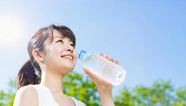 夏の空の下で水分補給をする女性 夏の空の下で水分補給をする女性の写真
