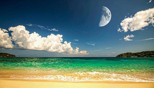 ビーチの青空に浮かぶ透けた白い月の写真