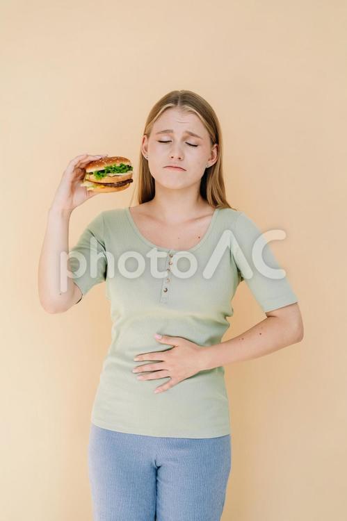 ハンバーガーを持ってお腹が痛い女性 女性,人物,ハンバーガーの写真素材