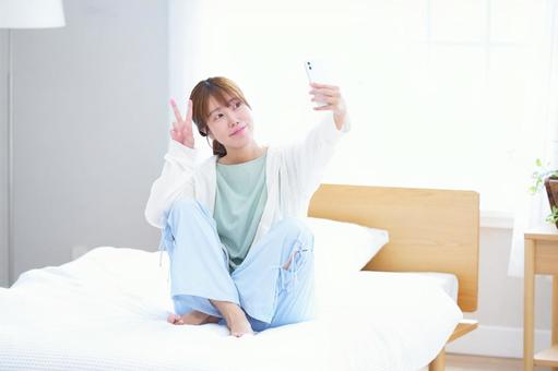 ベッドに座りピースする女性の写真