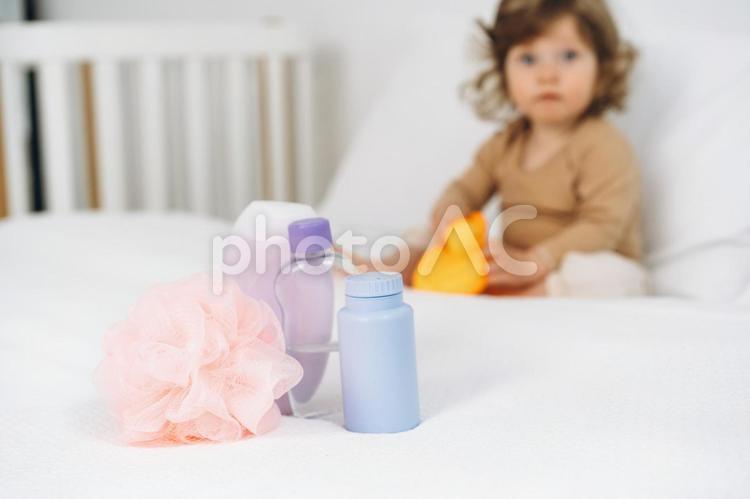 ベッドの上に置かれたバスグッズとお座りする子供 ベビー用品,スキンケア,バスグッズの写真素材