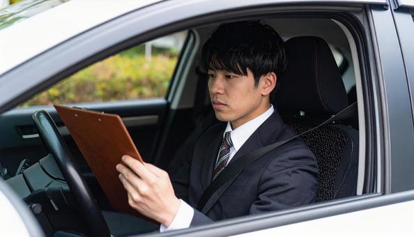 手もとに書類を持って運転するサラリーマン 手もとに書類を持って運転するサラリーマンの写真