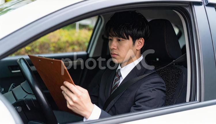手もとに書類を持って運転するサラリーマン サラリーマン,ドライバー,営業マンの写真素材