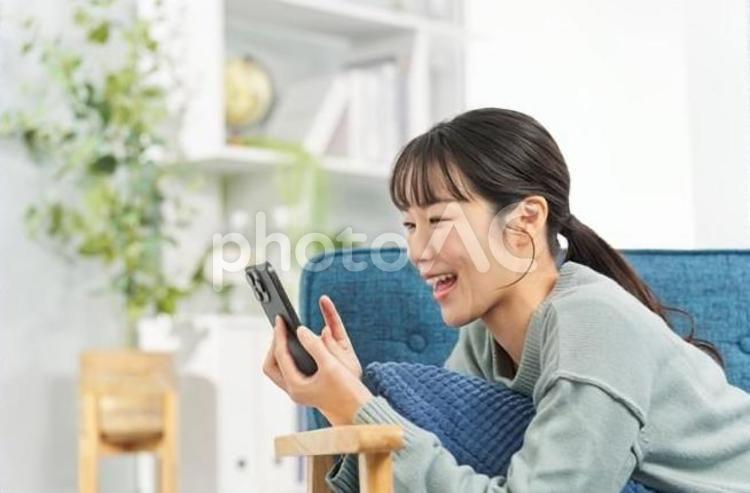 ソファで寝転んでスマートフォンを見る女性 女性,スマートフォン,ソファの写真素材