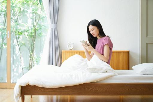 ベッドでスマホを操作中の黒髪女性 女性,スマートフォン,持つの写真素材