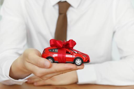 リボンを巻いた赤い車の模型を持つ手元 保険業,事務職,接客業の写真素材