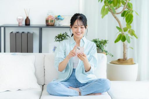 部屋でスマホを操作する若い女性 スマホ,笑顔,女性の写真素材
