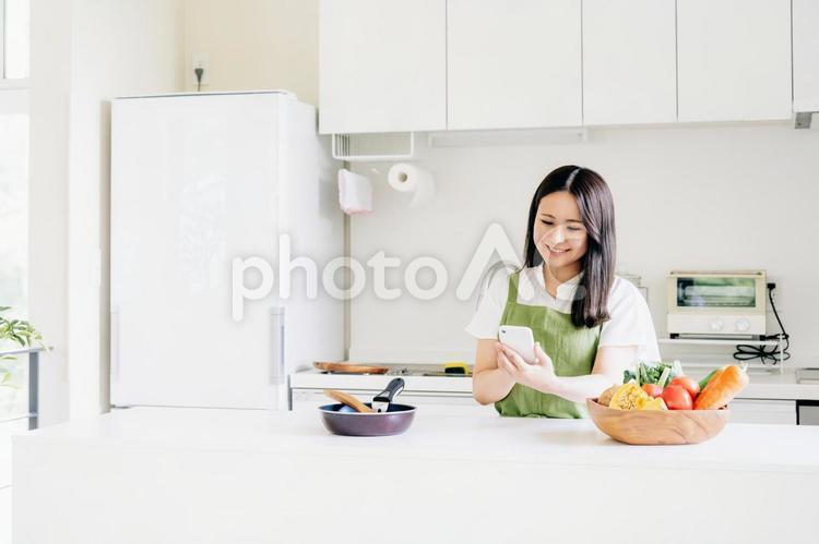スマホを見ながら料理する女性（笑顔） 料理,家事,スマホの写真素材