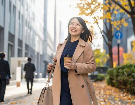 オフィス街を笑顔で歩く通勤中の女性 オフィス街を笑顔で歩く通勤中の女性の写真