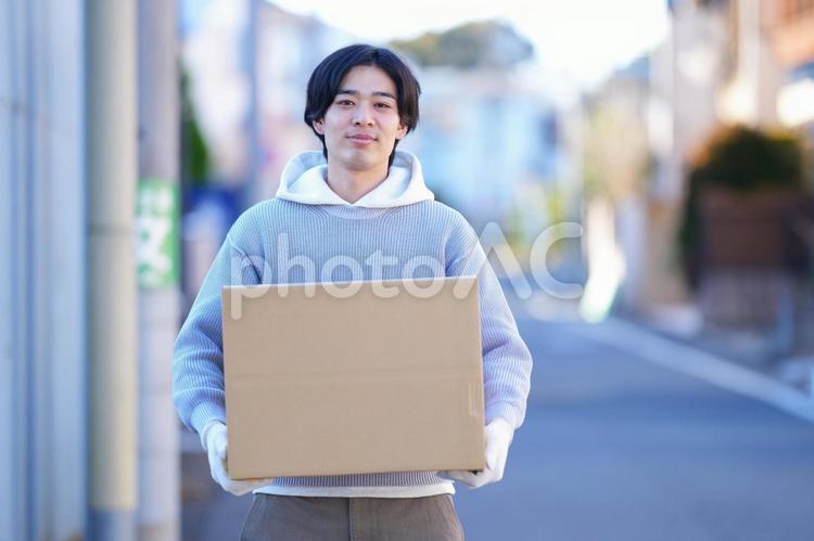 屋外で引っ越しの段ボール箱を持って立つ男性 引っ越し,一人暮らし,男性の写真素材