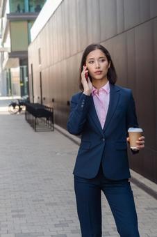 街なかでコーヒー片手に電話しているアジア人ビジネスウーマン ビジネスウーマン,ビジネス,女性の写真素材