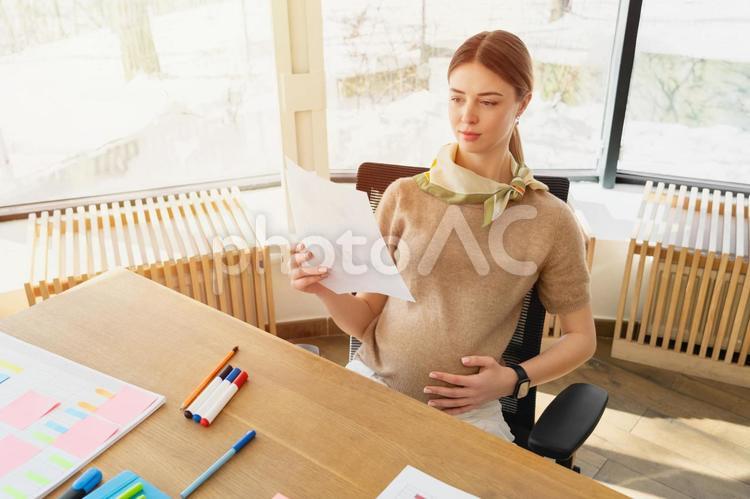 オフィスでお腹を触りながら資料を見ている妊娠中の女性 ビジネス,ビジネスウーマン,女性の写真素材