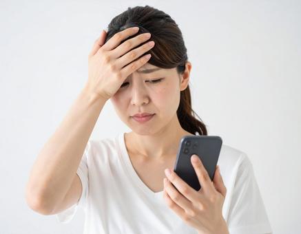 スマホを見て困惑する女性 スマホを見て困惑する女性の写真