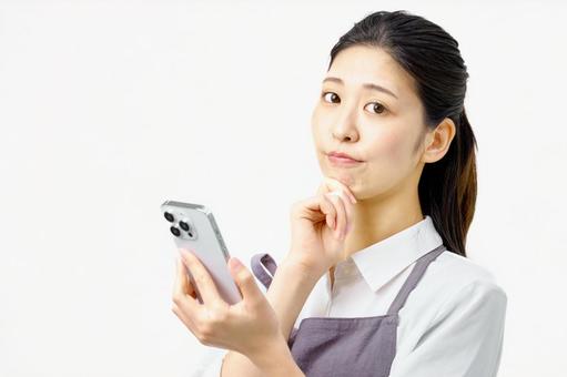 スマホを持ち考えるエプロンの女性 スマホを持ち考えるエプロンの女性 主婦,スマホ,考えるの写真素材