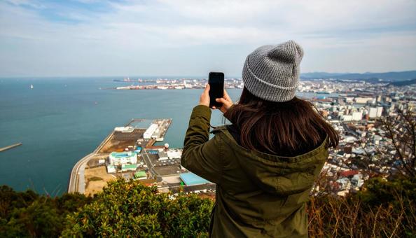 海の向こうを携帯で撮影する観光客の女性 海の向こうを携帯で撮影する観光客の女性の写真