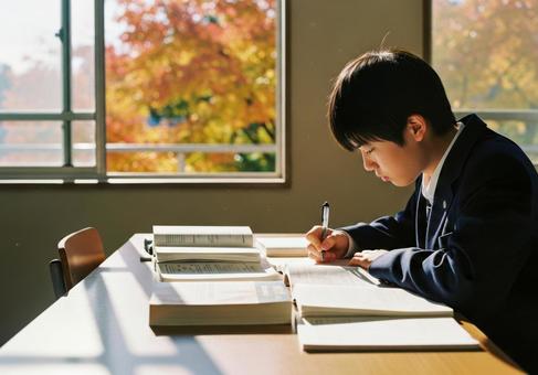 秋の教室で勉強に集中する男子学生の写真