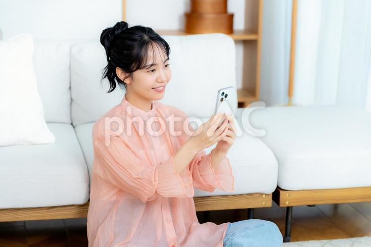 部屋でスマホを操作する若い女性 部屋でスマホを操作する若い女性 スマホ,若い女性,笑顔の写真素材
