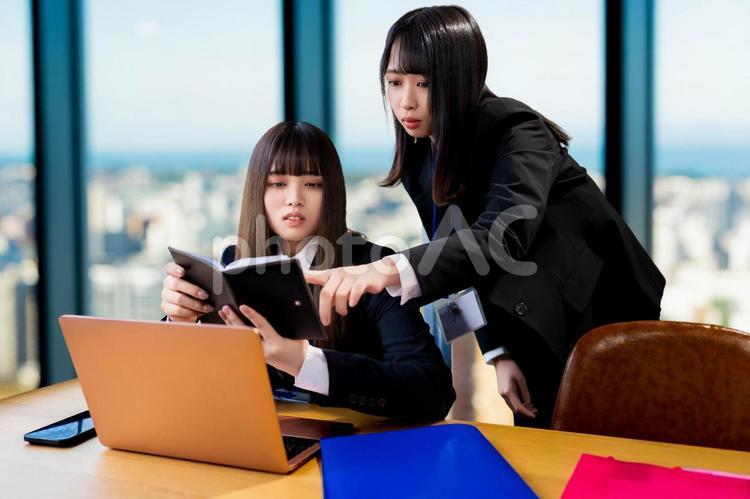 手帳を見て先輩に教えてもらう若い女性社員 女性,ビジネス,ビジネスウーマンの写真素材