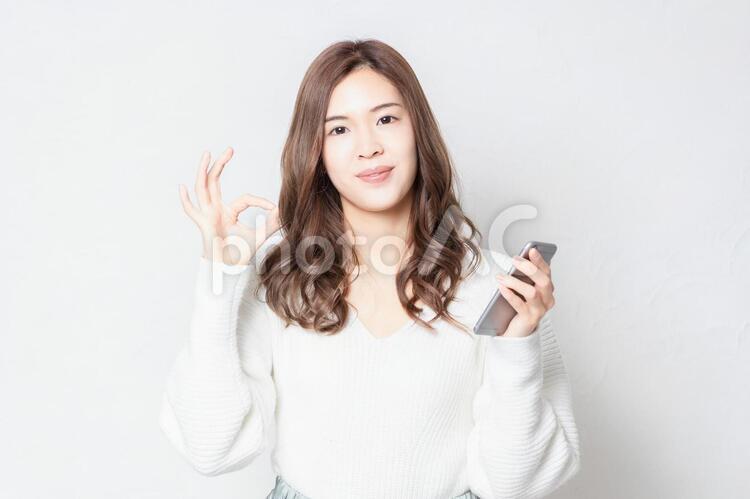 白い壁の前に立って、スマホを使う若い女性 女性,スマホ,snsの写真素材