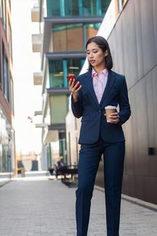 街なかでコーヒーとスマートフォン見ながら立っているビジネスウーマン ビジネスウーマン,ビジネス,女性の写真素材
