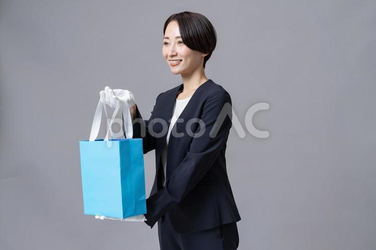  紙袋を渡すスーツを着た女性 販売員,ファッション,ジュエリーの写真素材